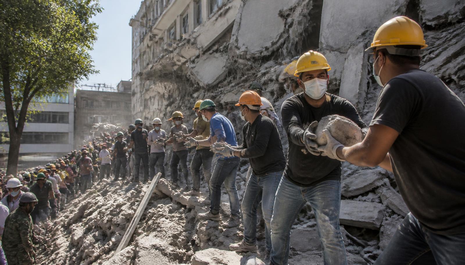 Rescue workers and volunteers in hard hats passing concrete rubble down a human chain beside a collapsed building in Cali, Colombia